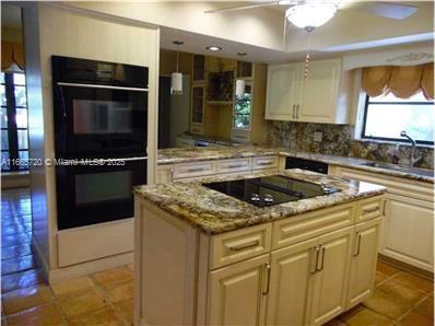 kitchen featuring sink, tasteful backsplash, light tile patterned floors, a kitchen island, and black appliances