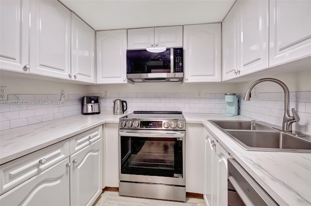 kitchen with appliances with stainless steel finishes, sink, tasteful backsplash, and white cabinetry