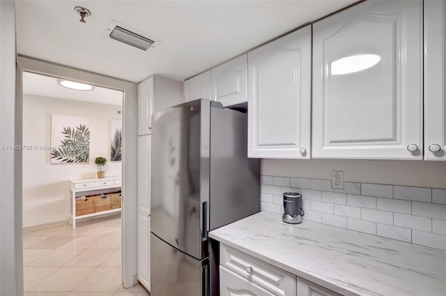 kitchen featuring light stone counters, stainless steel fridge, light tile patterned floors, and white cabinetry