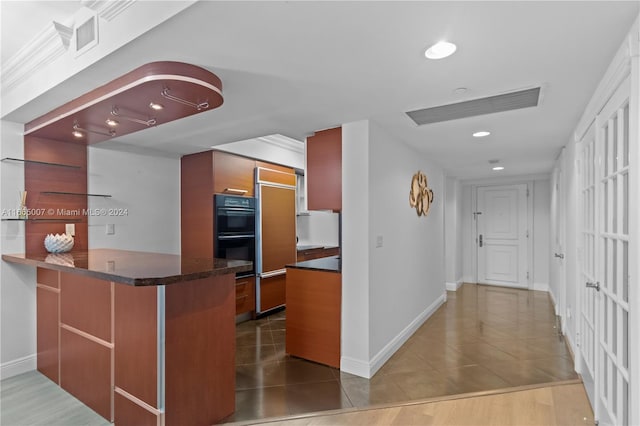 kitchen with paneled built in refrigerator, kitchen peninsula, black double oven, hardwood / wood-style flooring, and ornamental molding