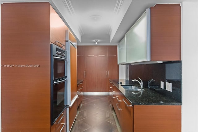 kitchen with dark stone countertops, backsplash, double oven, and sink