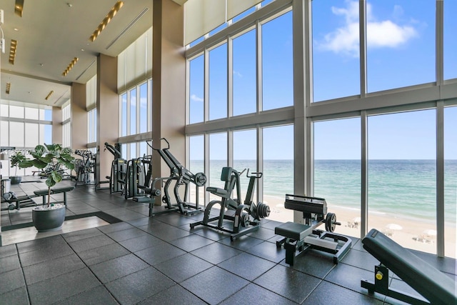 exercise room featuring a high ceiling, a water view, and a beach view