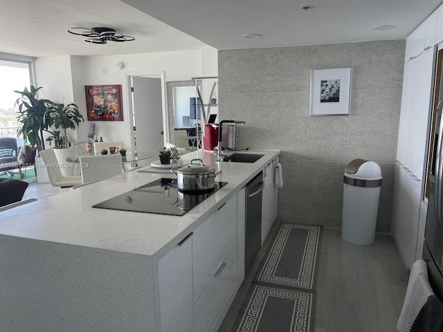 kitchen with black electric cooktop, tile walls, white cabinetry, dishwasher, and sink