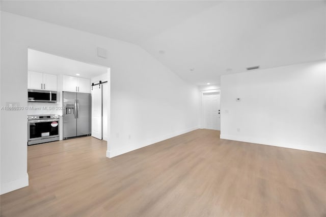 unfurnished living room featuring a barn door, lofted ceiling, and light wood-type flooring