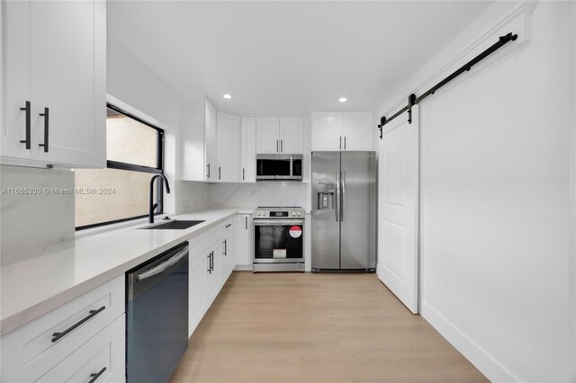 kitchen featuring light hardwood / wood-style floors, white cabinets, a barn door, stainless steel appliances, and sink