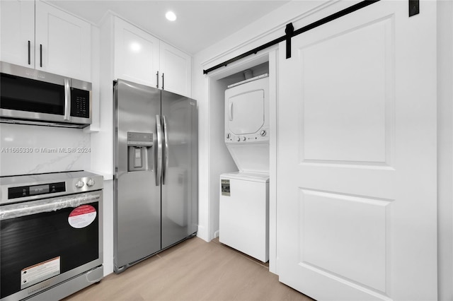 kitchen with stacked washing maching and dryer, white cabinets, a barn door, stainless steel appliances, and light wood-type flooring