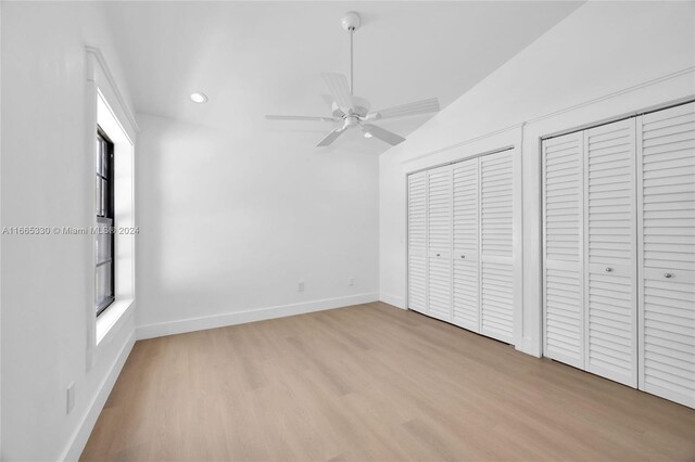 unfurnished bedroom with vaulted ceiling, two closets, ceiling fan, and light hardwood / wood-style flooring