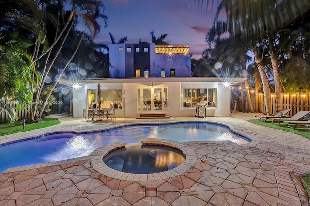 pool at dusk with an in ground hot tub and a patio area