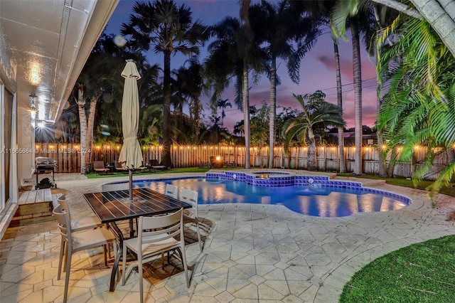 pool at dusk featuring an in ground hot tub and a patio area