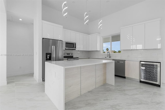 kitchen with sink, beverage cooler, white cabinets, a kitchen island, and appliances with stainless steel finishes