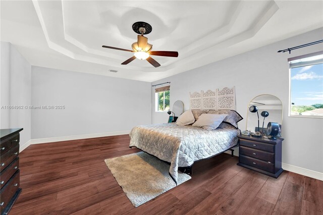 bedroom with dark hardwood / wood-style flooring, a tray ceiling, and ceiling fan