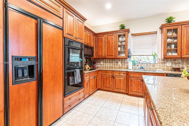 kitchen featuring light tile patterned floors, backsplash, light stone countertops, black appliances, and sink