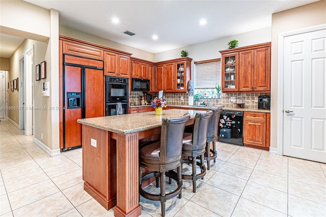 kitchen with decorative backsplash, a kitchen island, black appliances, light stone countertops, and light tile patterned floors