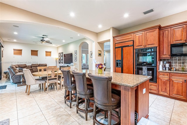 kitchen featuring a kitchen island, backsplash, black appliances, light stone counters, and ceiling fan