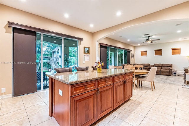 kitchen with a kitchen island, light stone countertops, light tile patterned flooring, and ceiling fan