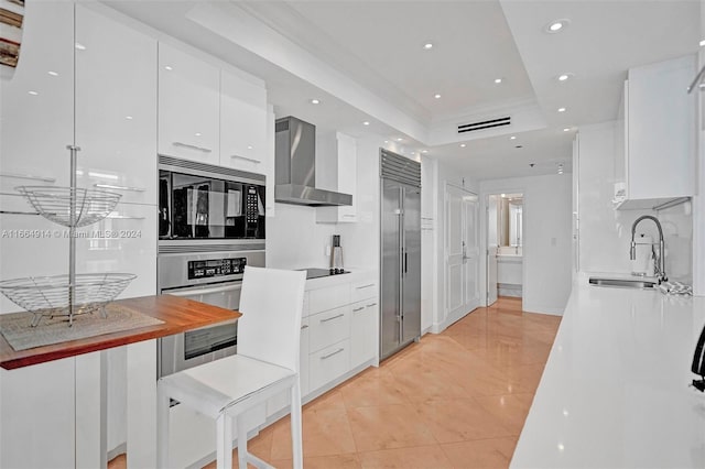 kitchen with light tile patterned flooring, sink, wall chimney range hood, white cabinetry, and built in appliances