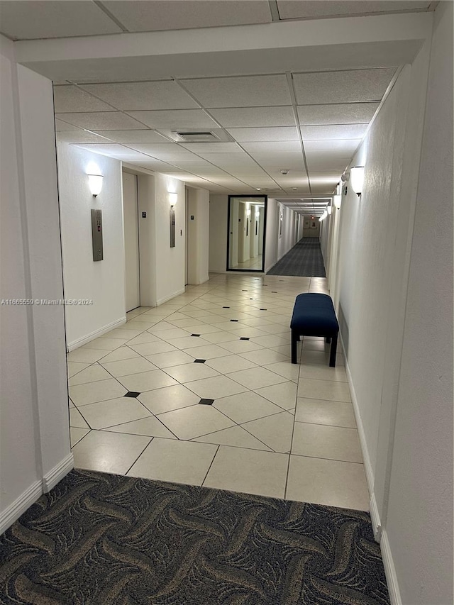 hall with elevator, light tile patterned floors, and a drop ceiling