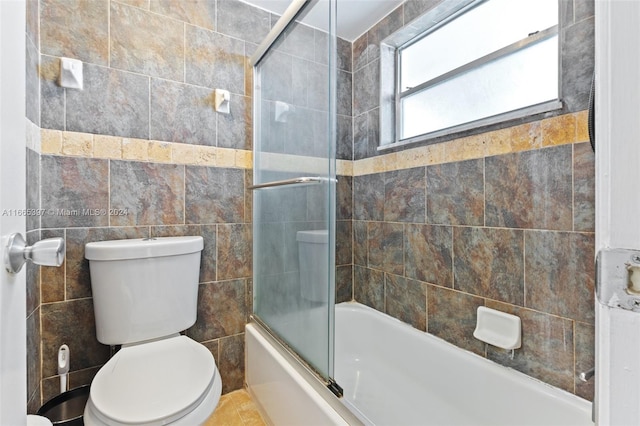 bathroom with tile walls, bath / shower combo with glass door, and toilet