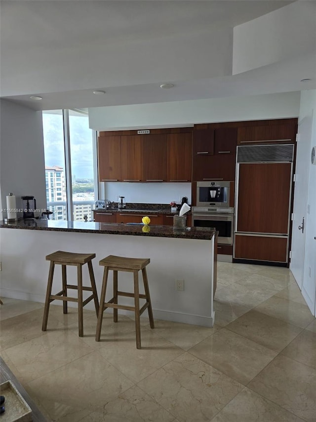 kitchen with kitchen peninsula, paneled built in fridge, a kitchen breakfast bar, dark stone countertops, and stainless steel double oven