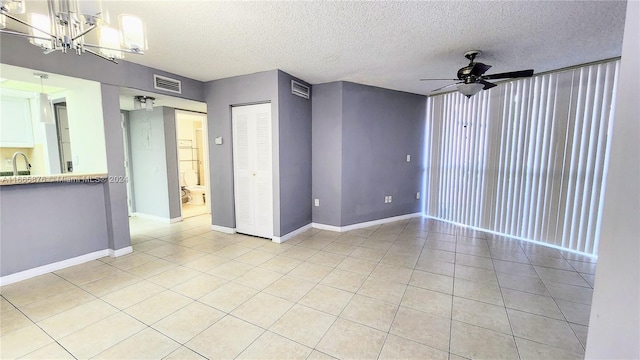 tiled empty room with a textured ceiling, ceiling fan with notable chandelier, and sink