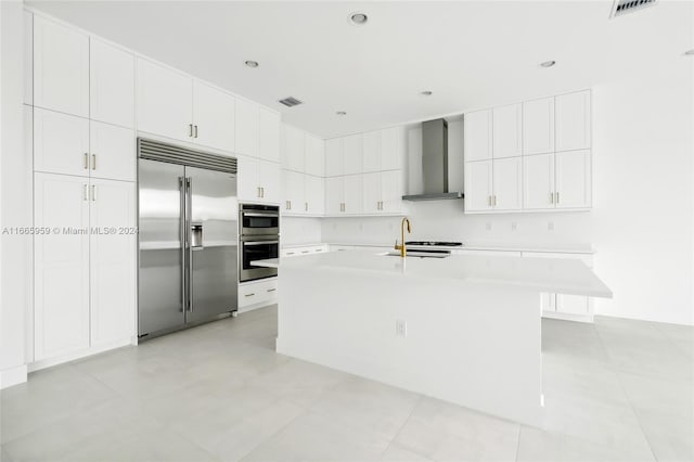 kitchen featuring an island with sink, white cabinetry, wall chimney range hood, and stainless steel appliances