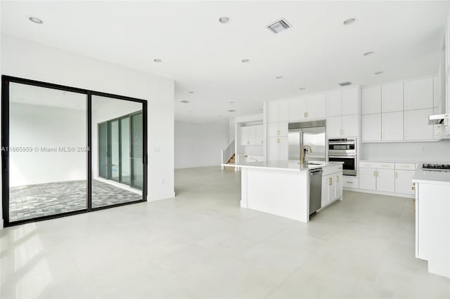 kitchen featuring sink, light tile patterned floors, a kitchen island with sink, white cabinetry, and appliances with stainless steel finishes