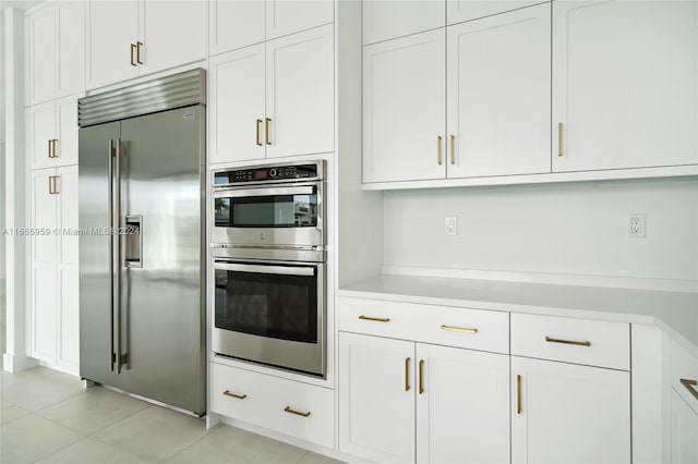 kitchen with appliances with stainless steel finishes, light tile patterned flooring, and white cabinets