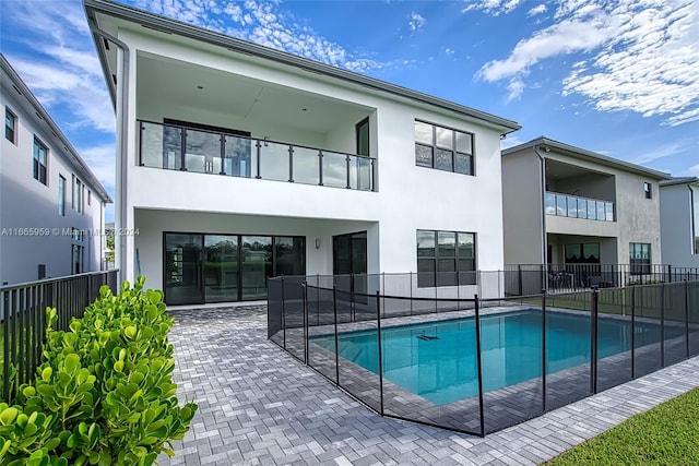 rear view of house with a balcony, a fenced in pool, and a patio area