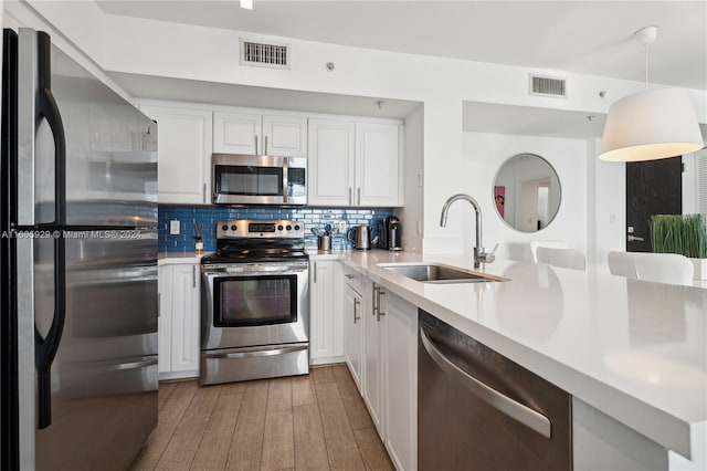 kitchen featuring sink, white cabinetry, hanging light fixtures, light hardwood / wood-style flooring, and stainless steel appliances