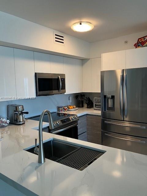 kitchen with white cabinets, kitchen peninsula, sink, stainless steel appliances, and light stone countertops