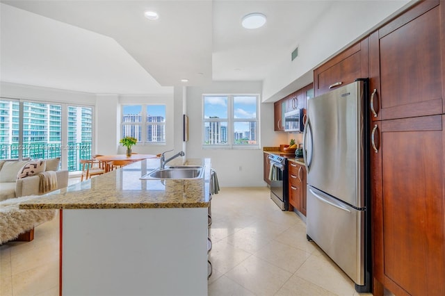 kitchen featuring light stone counters, an island with sink, stainless steel appliances, and sink