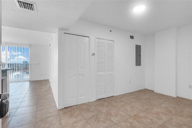 unfurnished bedroom with light tile patterned flooring, a textured ceiling, electric panel, and two closets