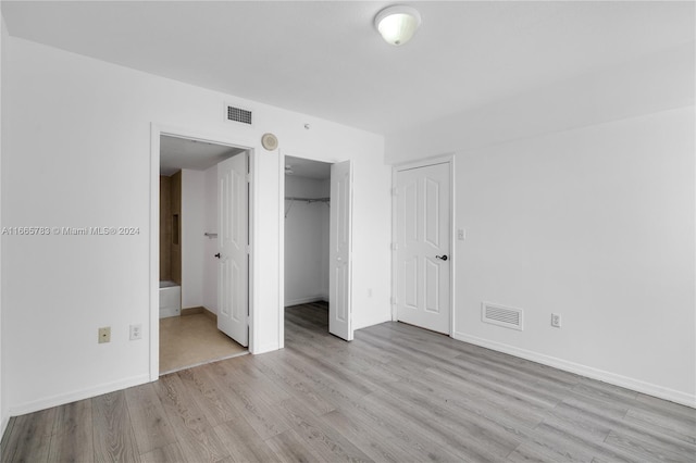 unfurnished bedroom with a closet, light hardwood / wood-style flooring, a spacious closet, and connected bathroom