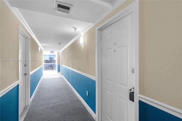 corridor with ornamental molding, carpet, and a textured ceiling