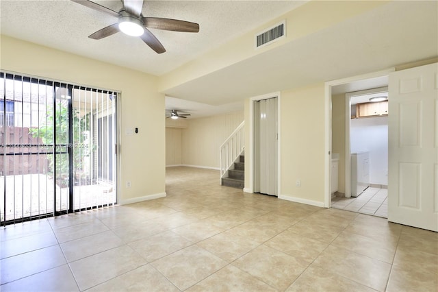 empty room featuring a textured ceiling, light tile patterned floors, washer / clothes dryer, and ceiling fan