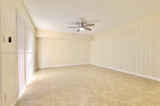 unfurnished room with ceiling fan, a textured ceiling, and wooden walls