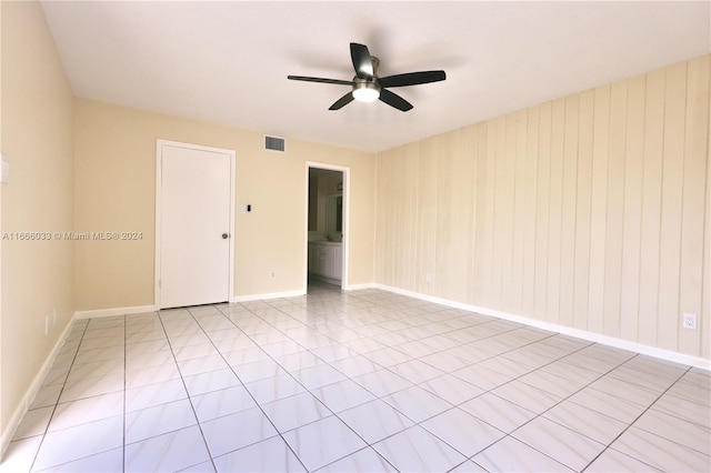 empty room featuring light tile patterned floors, wooden walls, and ceiling fan