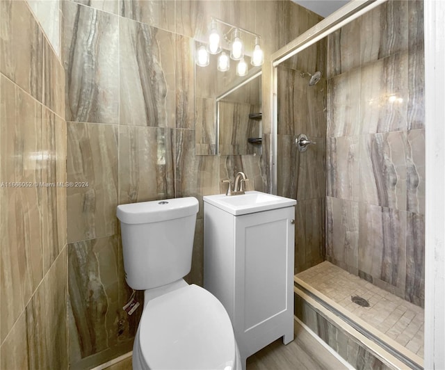 bathroom with a tile shower, vanity, tile walls, and toilet