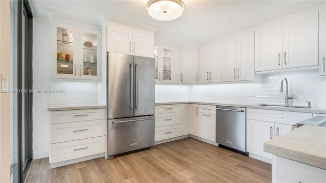 kitchen featuring sink, light hardwood / wood-style flooring, backsplash, white cabinetry, and appliances with stainless steel finishes