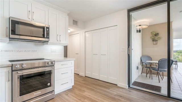 kitchen featuring white cabinets, appliances with stainless steel finishes, light wood-type flooring, and decorative backsplash