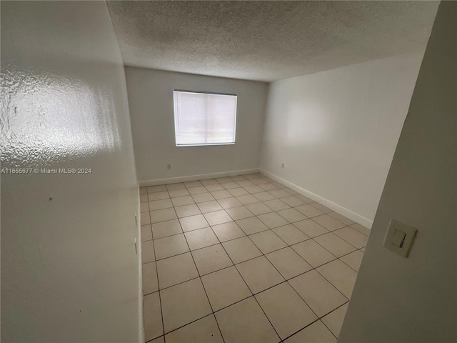 empty room with a textured ceiling and light tile patterned floors