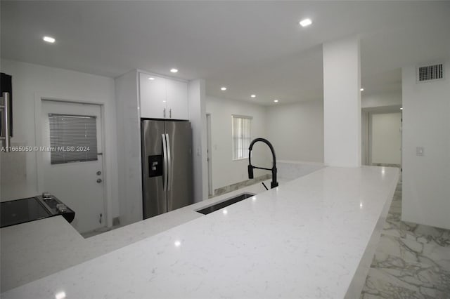 kitchen featuring sink, stainless steel refrigerator with ice dispenser, white cabinetry, black range oven, and light stone countertops