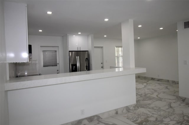 kitchen with stainless steel fridge, kitchen peninsula, and white cabinetry