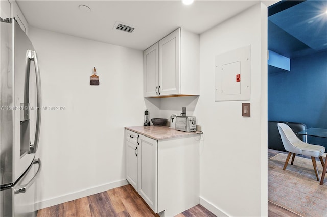 kitchen with white cabinets, electric panel, stainless steel fridge, hardwood / wood-style flooring, and light stone countertops