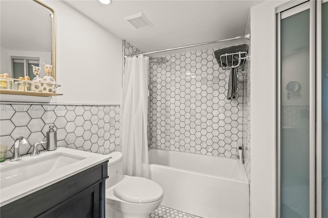 full bathroom with vanity, tile walls, visible vents, toilet, and shower / bath combo with shower curtain