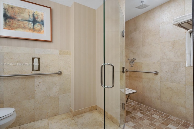 bathroom with tile walls, toilet, and a shower with shower door