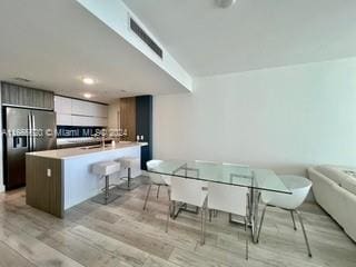 kitchen with stainless steel refrigerator with ice dispenser, a center island with sink, light wood-type flooring, and a breakfast bar