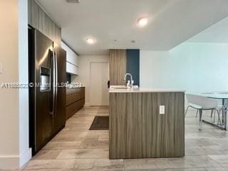 kitchen featuring stainless steel refrigerator with ice dispenser, a kitchen island with sink, sink, and light hardwood / wood-style flooring