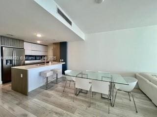 kitchen with black fridge with ice dispenser, visible vents, light wood-style flooring, a kitchen bar, and modern cabinets