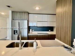 kitchen with a sink, stainless steel fridge with ice dispenser, visible vents, modern cabinets, and light countertops